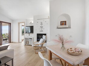 Ein modernes Wohnzimmer mit einer Couch, einem Esstisch mit einer Vase und einem Fernseher im Hintergrund.