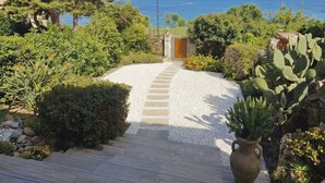 Un sentier qui mène à une porte d’où l’on peut admirer la mer et les montagnes en arrière-plan.