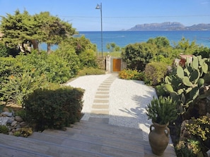 Ein Weg, der zu einer Tür führt, mit Blick auf das Meer und die dahinterliegenden Berge.