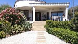 Une maison avec un toit incurvé, une véranda, un chemin de gravier menant à l’entrée et une petite table avec des chaises à l’extérieur.