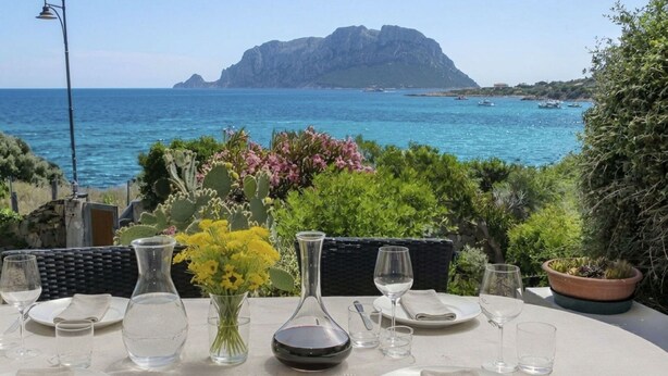 Une table dressée pour deux personnes, avec vue sur la mer et une montagne en arrière-plan.