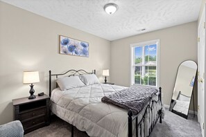 A bedroom with a bed, nightstands, a mirror, and a window with blinds.