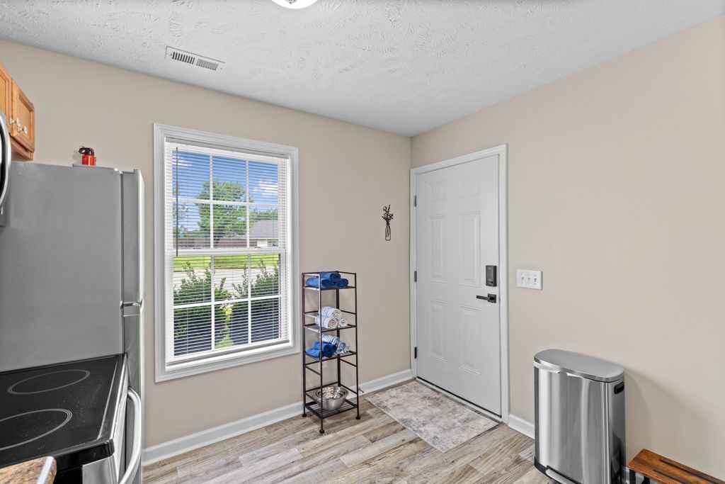 A kitchen with a refrigerator, a window with blinds, a door, and a trash can.