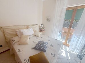 Un lit avec une couvre-lit à motifs marins, une table de chevet avec une lampe, et une vue sur l’extérieur à travers une porte vitrée.