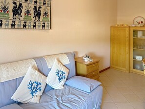 Une pièce comprenant un canapé, un meuble en bois avec des portes en verre et un mur orné d’une tapisserie décorative.