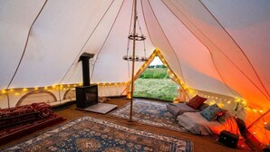 Interno di una tenda con un camino centrale, tappeti e vista sull'esterno.