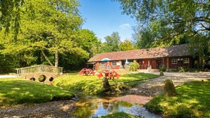 Un edificio rustico con tetto rosso, un ponte di legno e un piccolo ruscello.