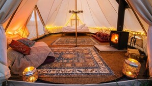 Interno accogliente di una tenda con un letto al centro, un camino a legna e tappeti decorati.