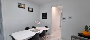 A dining area with a white table, black chairs, a flower vase, and framed pictures on the wall.