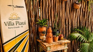 A surfboard with text, a bamboo wall, and potted plants.