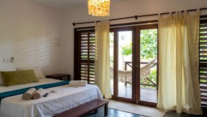 A hotel room with a bed, bedside table, a bench, a hanging light fixture, and a view of the outdoors through a sliding door.