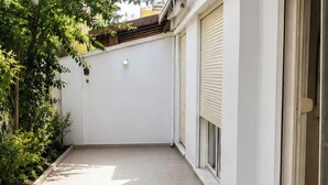 A covered outdoor area with tiled flooring, a white wall, and a door with a shutter. - Bubu Garden Apartament - 3 Bedrooms (Durres)