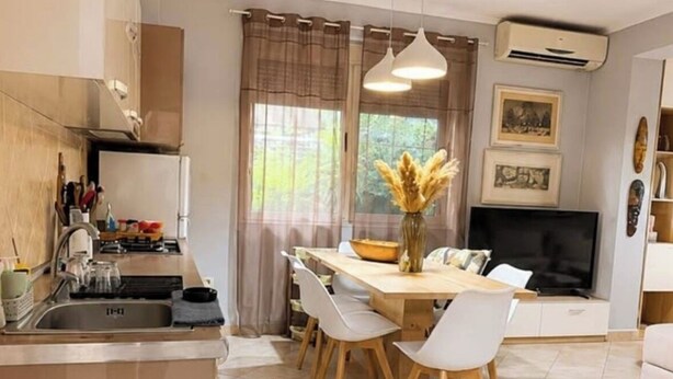 A modern kitchen with a central island, dining table with chairs, and a TV. - Bubu Garden Apartament - 3 Bedrooms (Durres)