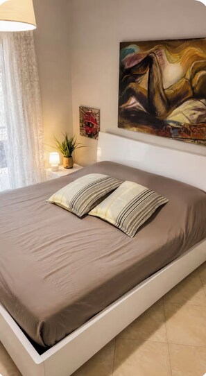 Une chambre à coucher moderne avec un grand lit, un tableau au mur et une lampe sur la table de chevet.