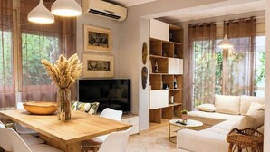 A modern living room with a sofa, a dining area with a wooden table and chairs, and a television. - Bubu Garden Apartament - 3 Bedrooms (Durres)