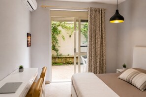 A bedroom with a bed, a desk, a chair, a hanging light, and a view of a garden through a sliding door. - Bubu Garden Apartament - 3 Bedrooms (Durres)