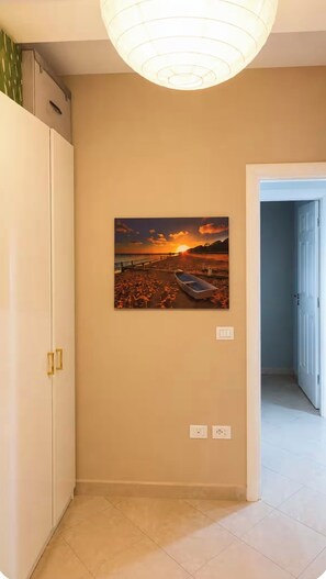 A hallway with a sunset painting on the wall, a white door, and a light fixture. - Bubu Garden Apartament - 3 Bedrooms (Durres)