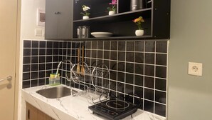 Keittiössä on mustilla laatoilla päällystetty seinäosa tiskialtaan yläpuolella, tiskiallas, astiateline ja kahvinkeitin, jotka on sijoitettu työtasolle.