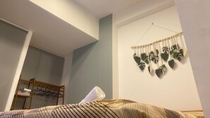 Makuuhuoneessa on sänky, puinen hylly, seinälle kiinnitetty makrame-kasviteline ja ikkuna.