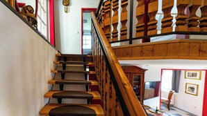 Eine Holztreppe mit Geländer, einer Uhr und Blick auf einen Essbereich darunter.