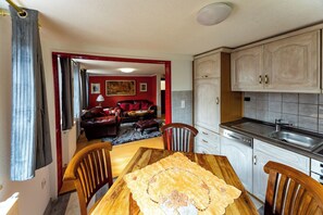 Un coin repas avec une table et des chaises en bois, une cuisine avec des meubles blancs et un évier, et un salon avec un canapé rouge et un tableau au mur.