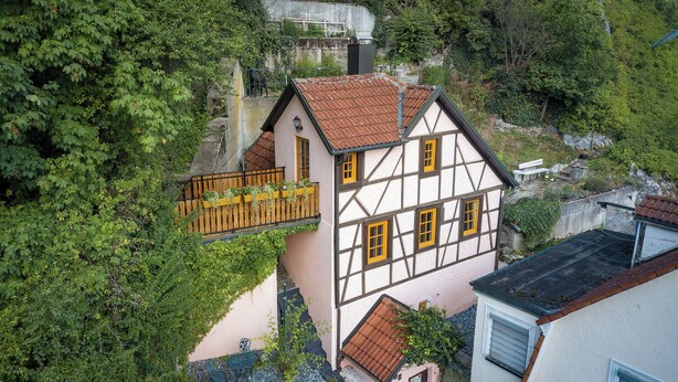 Ein traditionelles Fachwerkhäuschen mit Balkon, umgeben von üppigem Grün.