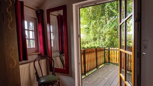 Ein Zimmer mit Holzstuhl, Heizkörper, Fenster mit roten Vorhängen und einem Balkon mit Holzboden und Geländer.