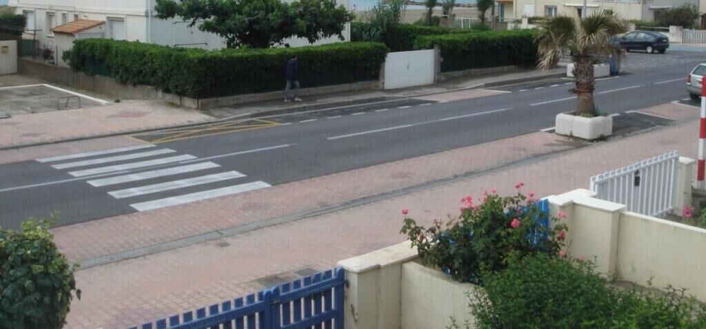 Une vue de rue avec un passage piéton, une porte bleue et une clôture blanche.