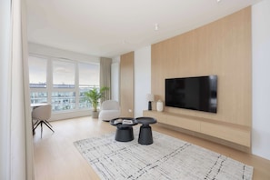 A modern living room with a large TV, two black coffee tables, a sofa, and a view of the city through large windows. - Spacious 3-Bedroom Apartment | Air Conditioning | Garage | Terrace (Warszawa)