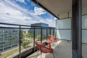 A balcony with two red chairs, a small table, and a large window offering a city view. - Spacious 3-Bedroom Apartment | Air Conditioning | Garage | Terrace (Warszawa)