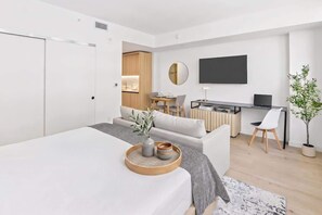 Ein modernes Hotelzimmer mit einem Bett, einem Schreibtisch, einem Sessel, einem Fernseher und einer Zimmerpflanze.