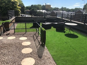 Un patio en la azotea con césped verde, zonas de estar circulares y barandilla de metal.