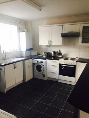 A compact kitchen with a washing machine, stove, and cabinets. - The Poacher (Stevenage)