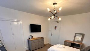 A hotel room with two beds, a television, a dresser, and a chandelier.