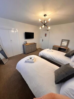A hotel room with two beds, a television, a dresser, and a chandelier.