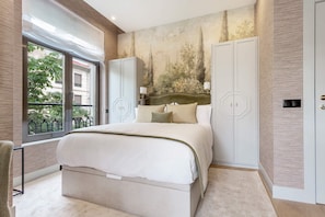 Ein Schlafzimmer mit einem großen Bett, einem Kleiderschrank, einem Spiegel und einem Fenster mit Blick auf Grünflächen.