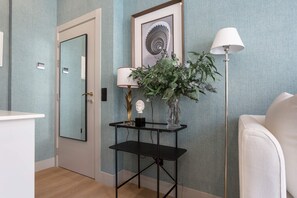 Ein Zimmer mit Tür, einem gerahmten Kunstwerk, einem Tisch mit Lampe und Vase sowie einer Stehlampe.
