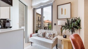 Un salon moderne avec un canapé, une machine à café, une lampe et une vue sur les immeubles à travers une porte vitrée.