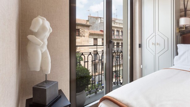 Une chambre d’hôtel avec un lit, une sculpture, une vue sur des immeubles et une porte.
