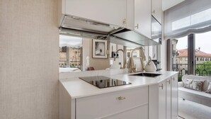 Une cuisine moderne avec des armoires blanches, une cuisinière encastrée et une vue sur la ville grâce à de grandes fenêtres.