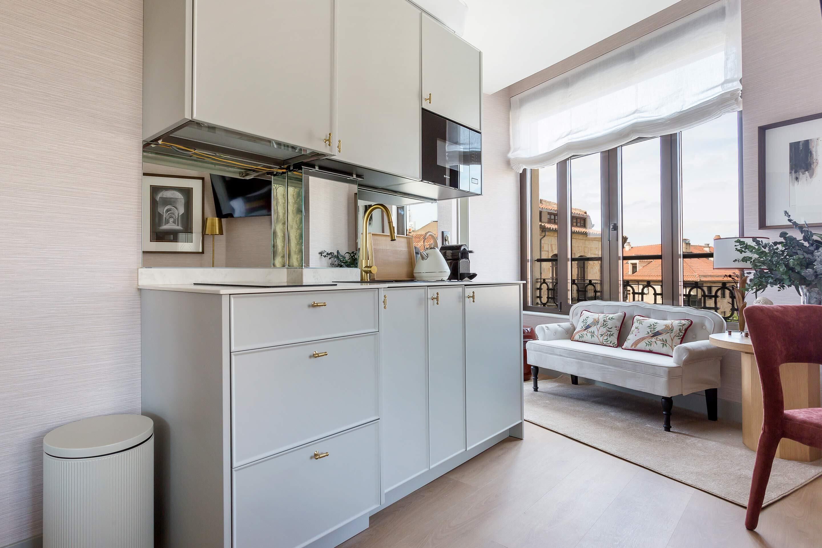 Una cocina moderna con gabinetes blancos, una campana extractora de acero inoxidable y un amplio ventanal con vistas a un paisaje urbano.