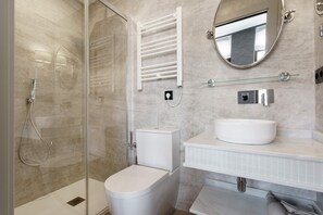 Een moderne badkamer met een douchecabine van glas, een wit toilet, een wastafel met spiegel en een handdoekhouder.
