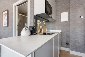 Een moderne keuken met een wit aanrecht, een ingebouwde kookplaat, een gouden kraan en grijs gestructureerde wanden.