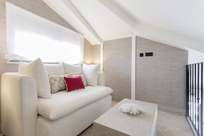 Een moderne woonkamer met een witte bank, een bijzettafeltje en een raam met lichtgordijnen.