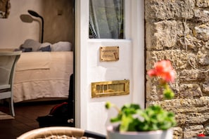 Ein Zimmer mit einem Bett, einem Fenster mit Namensschild, einer Steinwand und einer Topfpflanze.