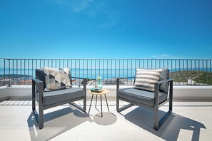Ein Balkon mit zwei grauen Sofas, einem kleinen runden Tisch und Blick auf das Meer.