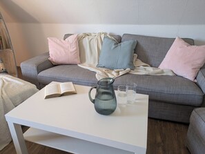 Un salon avec un canapé gris, une table basse blanche, un livre, un pichet en verre et deux verres.
