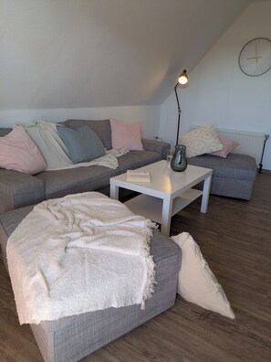 A modern living room with a sectional sofa, a coffee table, and a lamp. - Vacation apartment near the North Sea coast (Großheide)