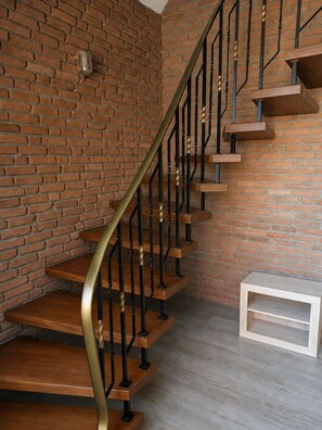 Un escalier avec des marches en bois et des rampes en métal noir, adossé à un mur de briques.