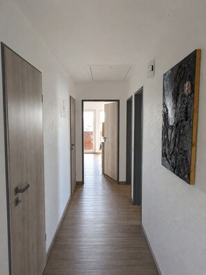Un couloir doté d’un plancher en bois, de murs blancs et d’un grand tableau abstrait sur le mur de droite.